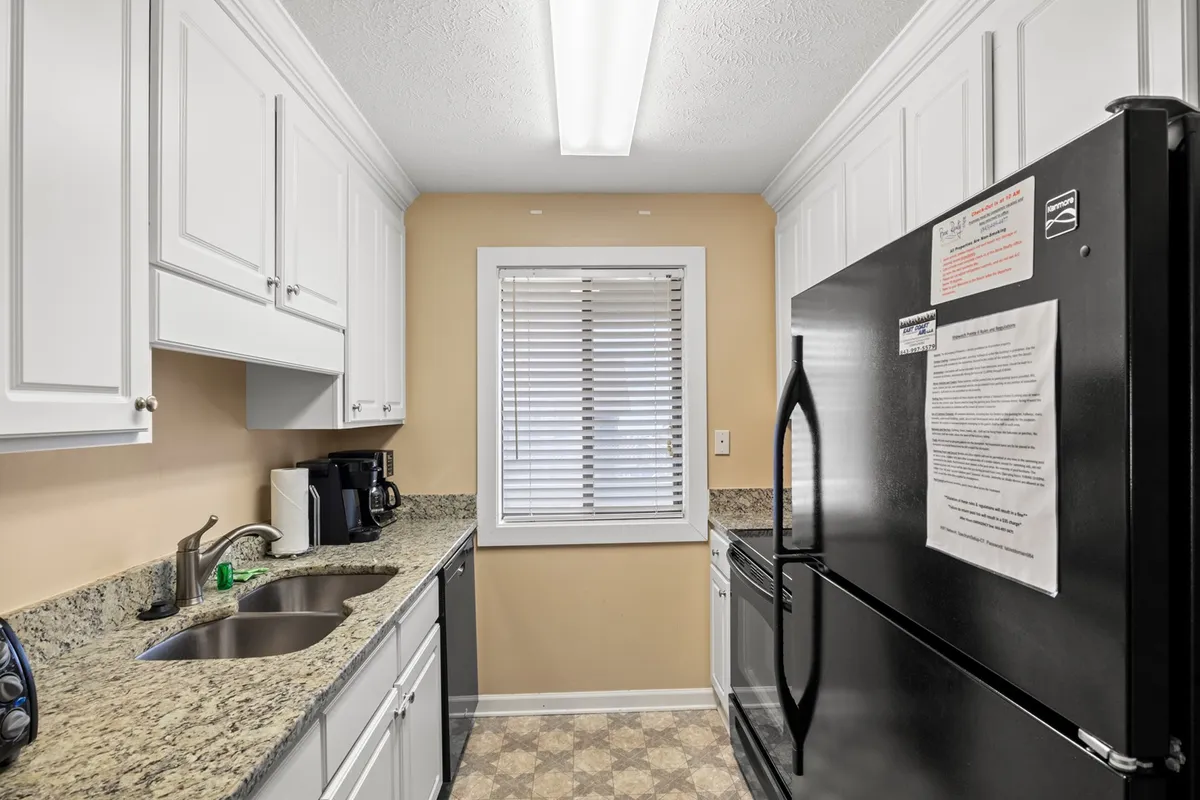 A detail view of the kitchen's granite countertop, a black refrigerator, and a window with blinds. The scene is practical and welcoming, emphasizing both the utility and comfort of the space.