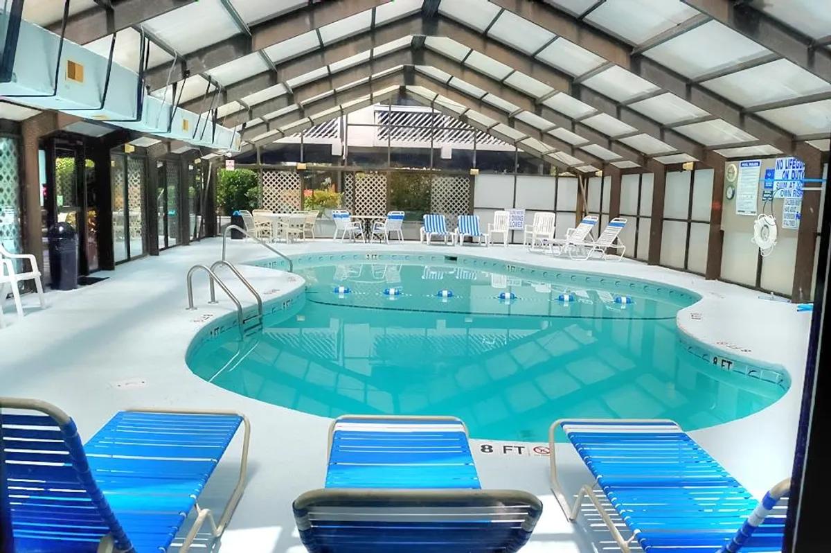 A bright, airy indoor swimming pool area with lounge chairs lined up alongside the water and large windows letting in natural light. The space feels cheerful and welcoming, offering a perfect retreat for all-weather swimming.
