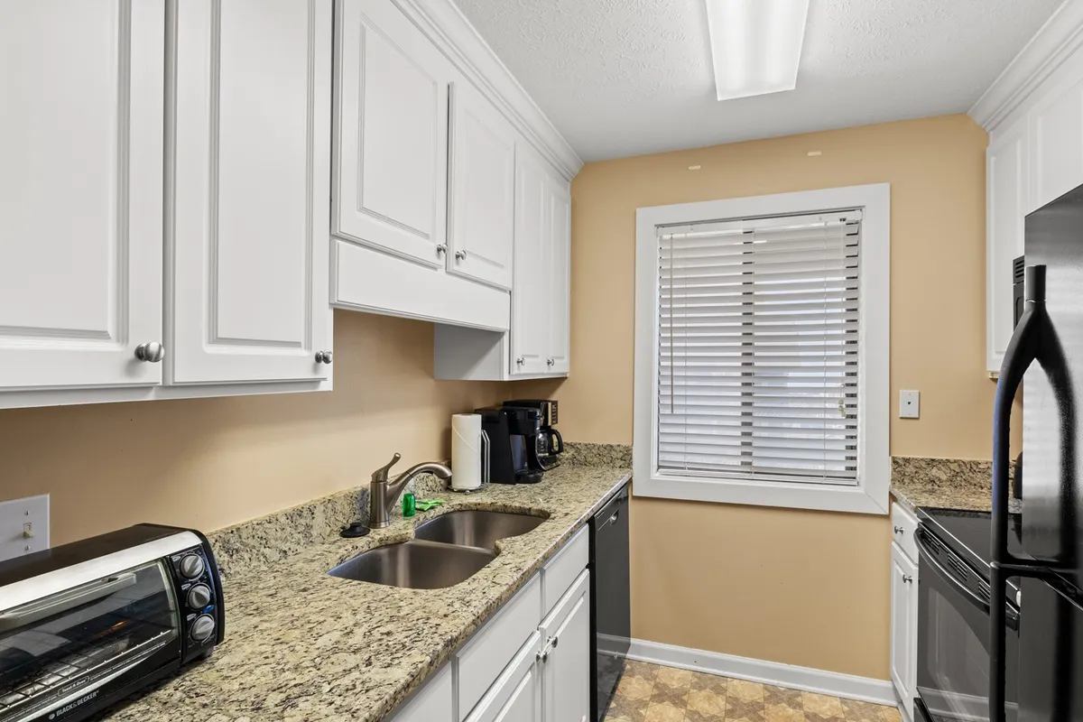 A modern kitchen with sleek granite countertops, dual sink, black appliances including a refrigerator and oven, and a window with blinds allowing in natural light. The layout is both functional and inviting, with plenty of counter space for meal prep and cooking activities.