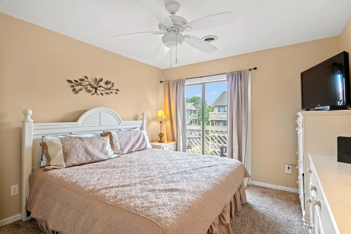 A serene bedroom featuring a plush bed with soft linens, a window allowing natural light to gently filter in, a bedside lamp, tasteful wall art, and a television for evening relaxation. The space exudes calm and comfort, ideal for unwinding after a busy day.
