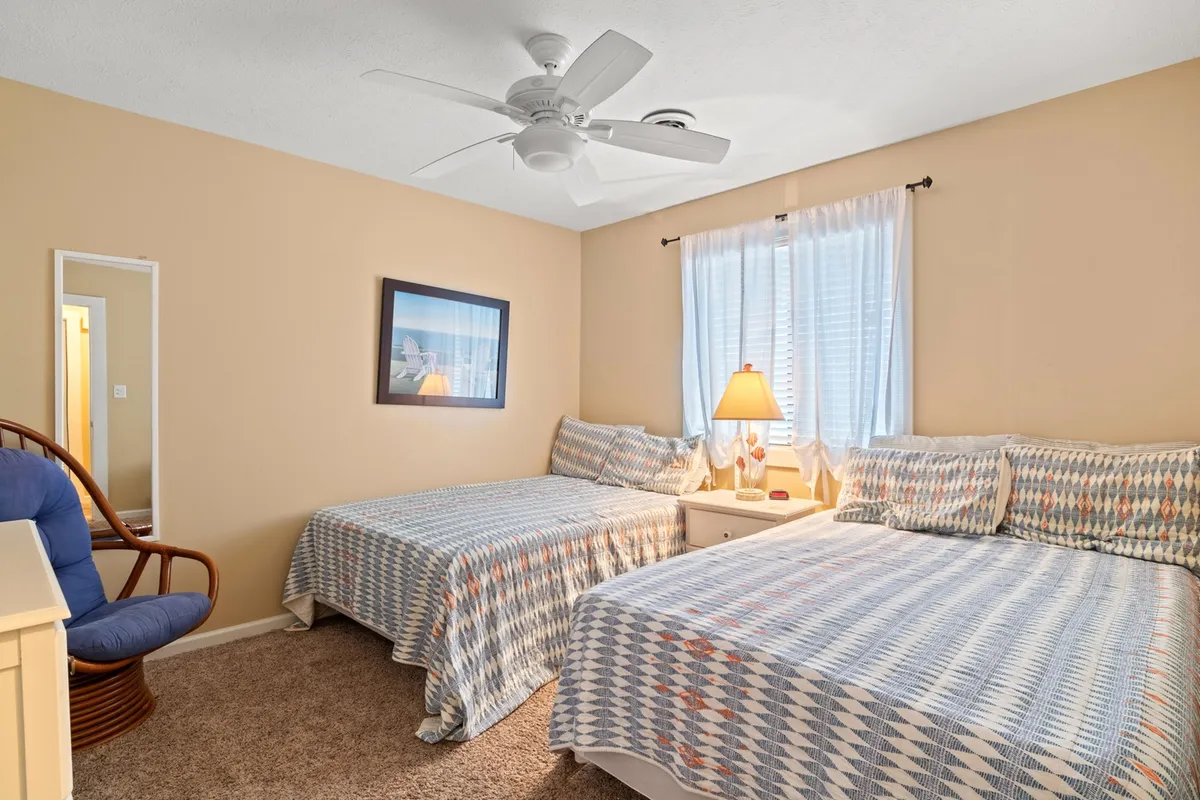 A cozy bedroom scene with two beds, a lamp between them, wall art above, and a mirror adding depth to the space. The arrangement creates an intimate setting ideal for relaxed conversations or quiet moments before sleep.