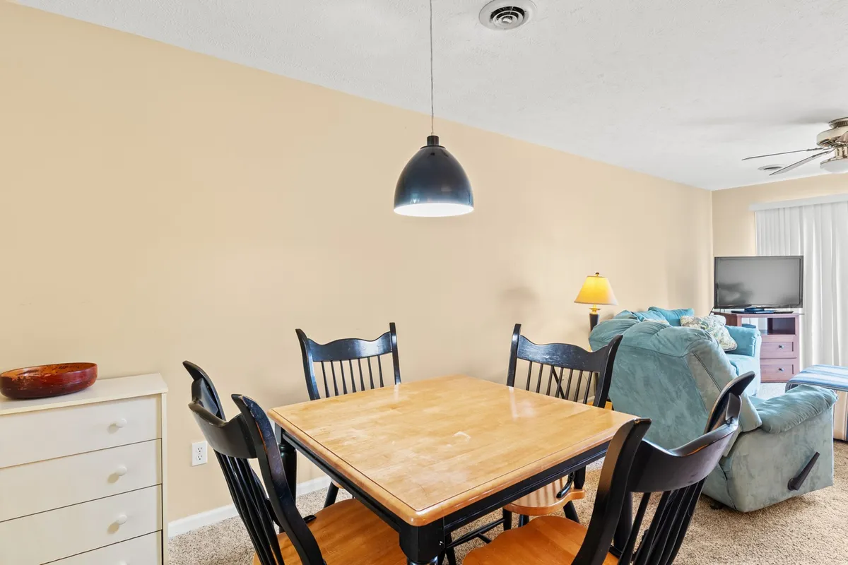 This image zeroes in on the dining area, featuring a welcoming dining table with blue chairs and a lamp, positioned near the television. The scene is set for family feasts, game nights, or intimate conversations.