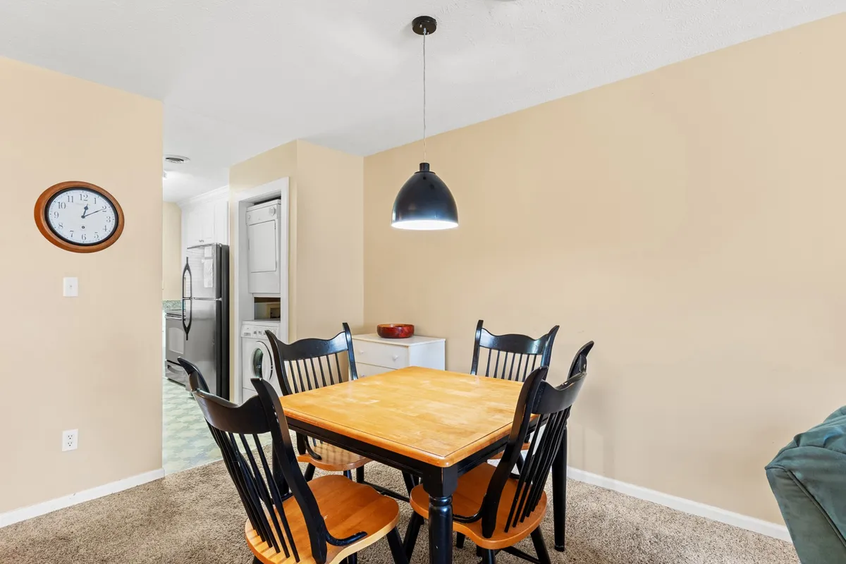An inviting dining area with a contemporary dining table surrounded by black chairs, softened by the glow of a pendant light and accented by a wall clock. The setup suggests a space designed for family meals and casual get-togethers.