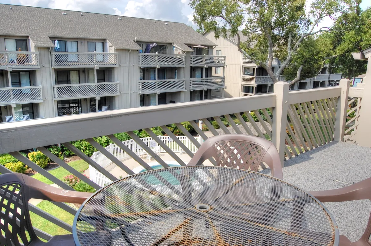 This image captures a welcoming outdoor balcony area overlooking a vibrant pool space. The outdoor table and balcony railing set a cozy scene, while the view of the pool suggests opportunities for relaxation, group gatherings, and enjoying morning coffee or evening chats outdoors.