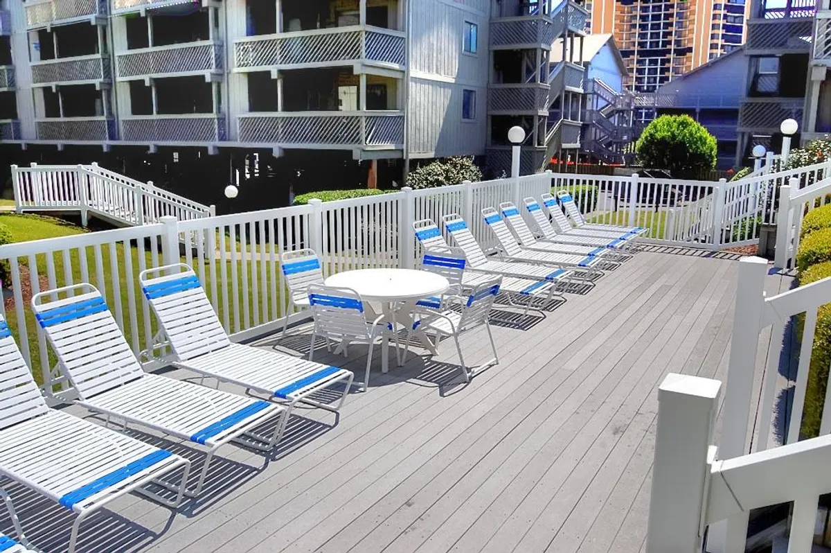 A sunlit poolside area featuring loungers, a white railing, and a table, set for relaxation and socializing. The inviting setting emphasizes the resort's amenities available for unwinding after a day of exploration.
